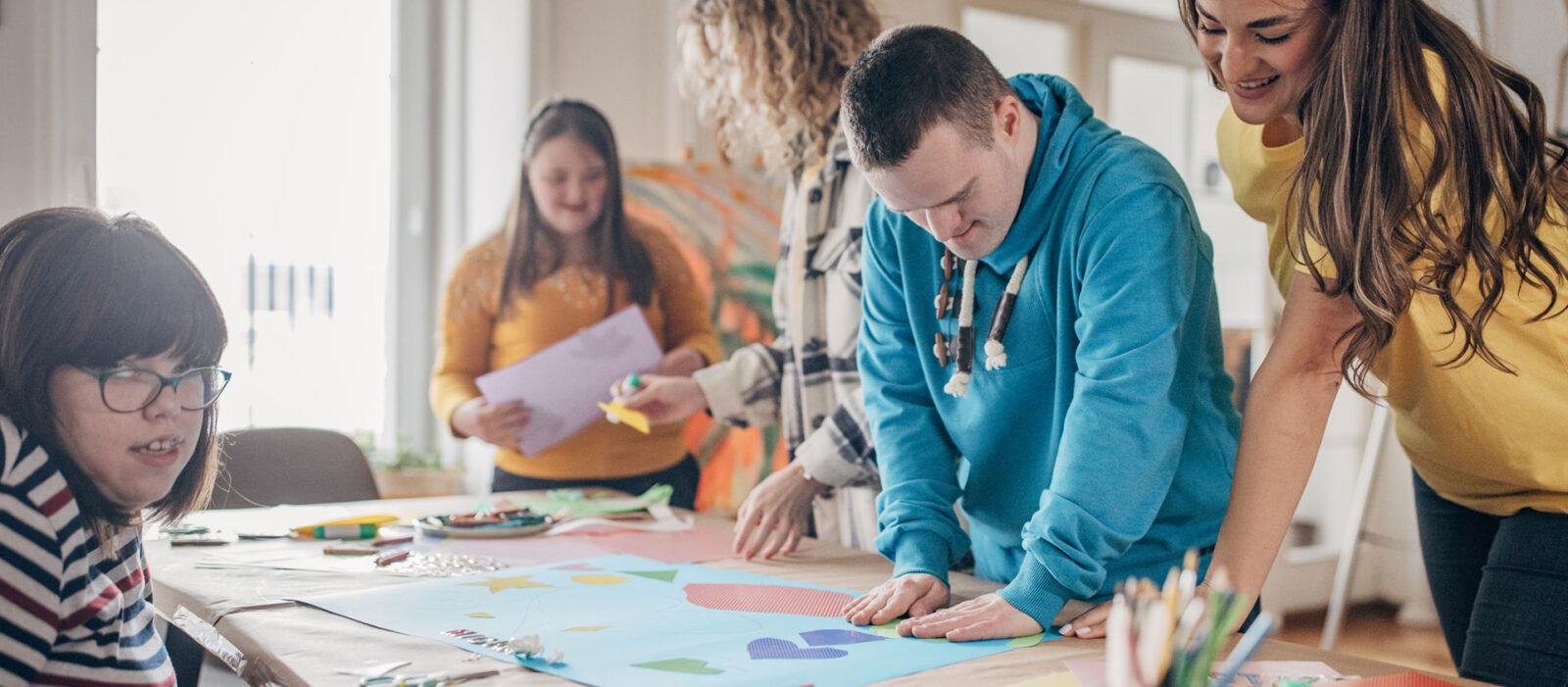People with down syndrome and cerebral palsy doing an art project with help with assistants and animators. Disability health care art workshop.